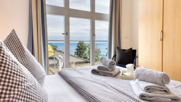 Habitación de hotel con cama, vista al mar y balcón con una silla y una mesa.