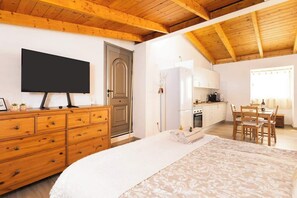 Ein Schlafzimmer mit Bett, Holzkommode, Fernseher und einer Küchenzeile mit Esstisch.