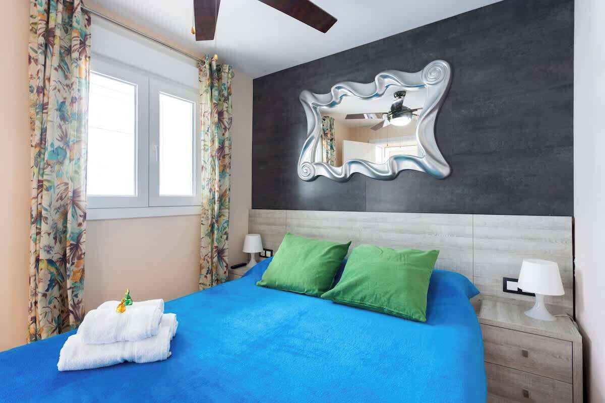 Ein Schlafzimmer mit einem Bett, zwei Kissen, einem Nachttisch, einem Spiegel und Vorhängen.