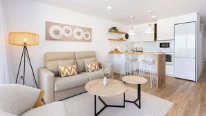 A modern living room with a sofa, coffee table, and a dining area with chairs. - Beachfront Luxury Apt w/ Sea Views & Pool Access (Puerto de la Cruz)