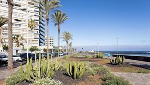 A coastal urban area with tall buildings, palm trees, cacti, and a clear blue sky. - Beachfront Luxury Apt w/ Sea Views & Pool Access (Puerto de la Cruz)