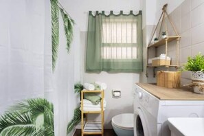 Ein kleines Badezimmer mit Waschmaschine, einem Holzboden mit Handtüchern und einem Fenster mit grüner Vorhang.