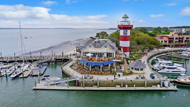 Ein Anwesen am Wasser mit einem Leuchtturm, angestaute Booten und einem Restaurant mit Terrassensitzplätzen.