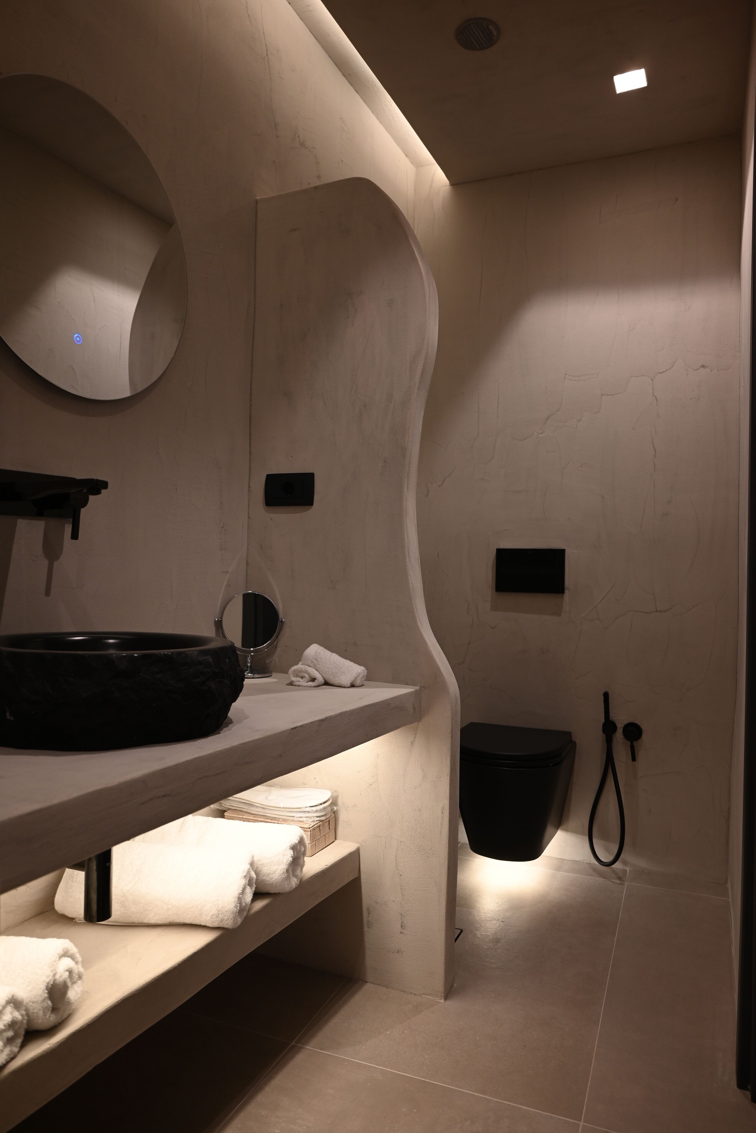 Une salle de bain moderne avec un lavabo aux lignes courbes, un miroir, un porte-serviettes et des toilettes noires.