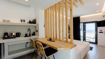 A modern hotel room with a wooden partition, a small kitchen area, a bed, and a balcony with a view.