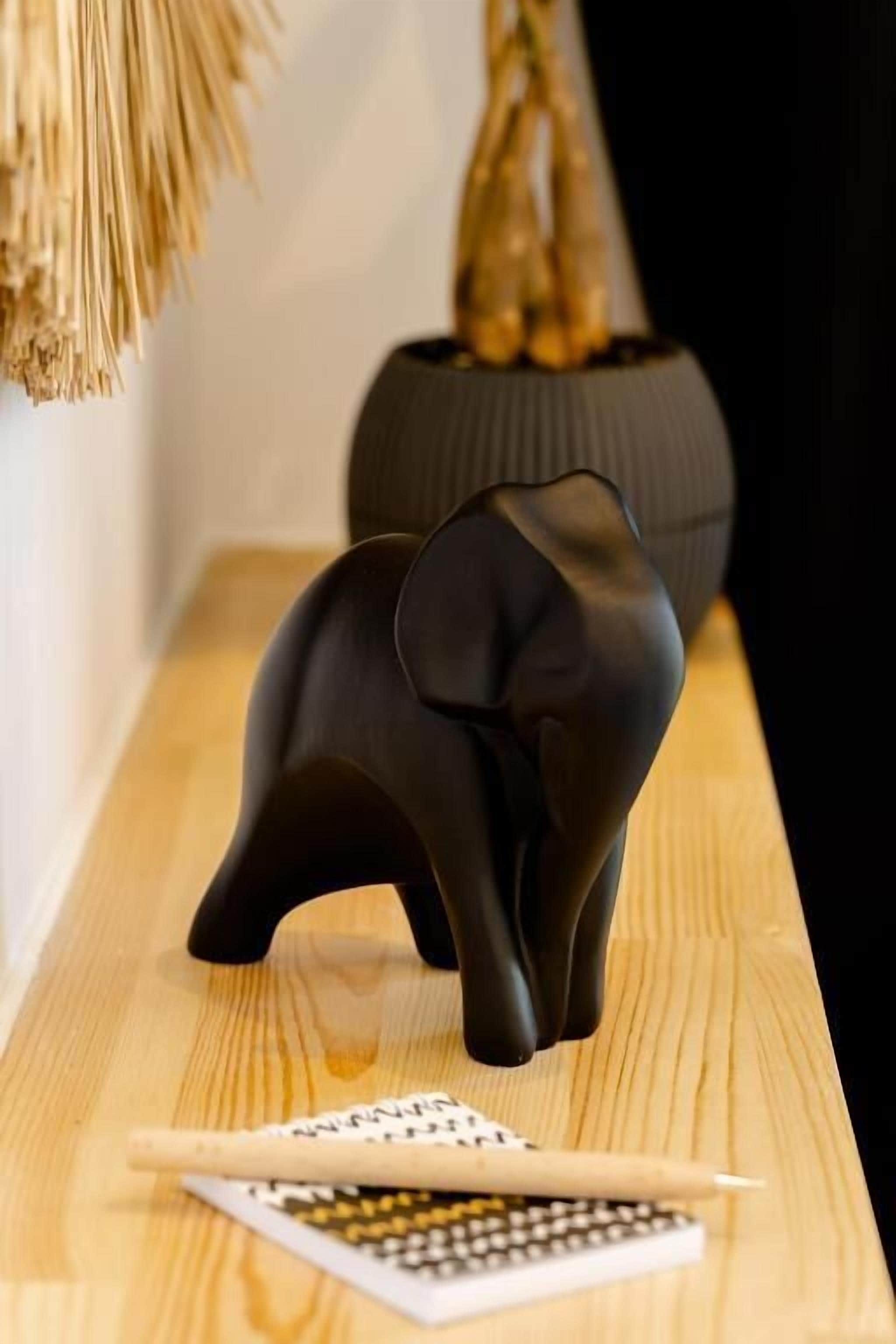 Un objet noir en forme d’éléphant, posé sur une surface en bois, avec une calculatrice et des dés à proximité.