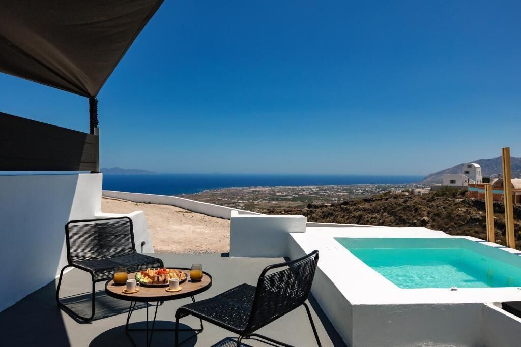 Eine Terrasse mit Pool, zwei Stühlen, einem Tisch mit Frühstück und Blick auf das Meer und die Stadt.