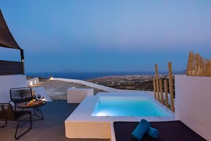 A rooftop terrace with a hot tub, seating area, and a view of the coastline. - Lackos Luxury Suites (Santorini)