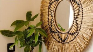 Een wand met een geweven spiegel, een potplant, een klein beeldje en een handdoek op een houten plank.