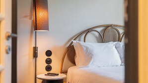 A neatly made bed with white linens, a bedside lamp, and a small table with a remote control. - Liiiving in Porto - Casa Duque Apt I (Porto)