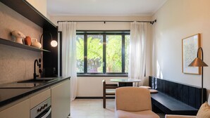 A modern kitchen with a dining area, a sofa, and a view of greenery outside. - Liiiving in Porto - Casa Duque Apt I (Porto)