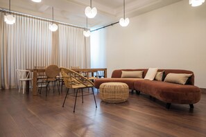 A modern living room with a wooden dining table, wicker chairs, a brown sofa, and hanging pendant lights. - Liiiving in Porto - Casa Duque Apt I (Porto)