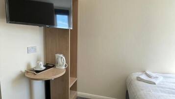 Habitación de hotel con cama, una mesita con hervidor y taza, un televisor montado en la pared y un armario de madera.