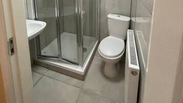 Ein kleines Badezimmer mit Duschkabine, weißer Toilette und Waschbecken auf Säule.
