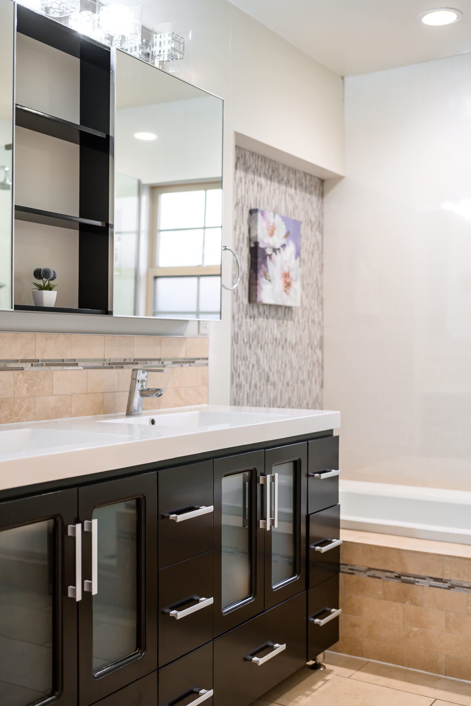 A modern bathroom with a large mirror, dark cabinets, a white sink, and a shower area.