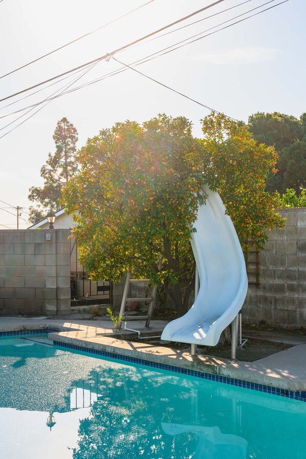 Una piscina con tobogán, rodeada de un muro de piedra y árboles.