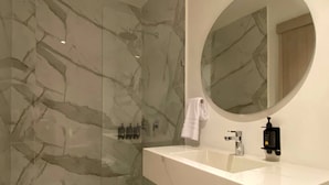 Un baño moderno con pared de mármol, un lavamanos blanco, un espejo redondo y una toalla colgada en la pared.
