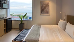 Habitación de hotel moderna con una cama grande, un escritorio con ordenador, una planta en maceta, una obra de arte enmarcada y vistas al mar.