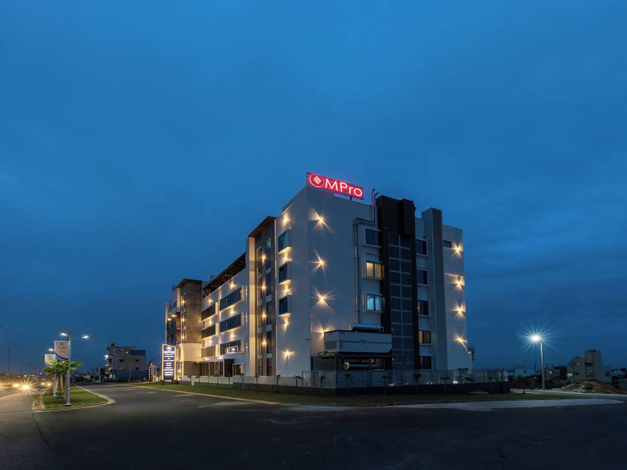 Un hotel de varios pisos con un llamativo letrero 'MPro' en el techo, con un diseño arquitectónico moderno, ventanas regularmente espaciadas y una fachada plana.