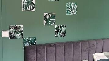 Un dormitori amb una paret verda, un capçal de llit amb textura i diverses obres d'art quadrades a la pared.