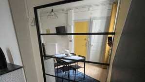 Une pièce comprenant un coin repas, une cloison à cadre noir et, au fond, une porte jaune.