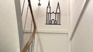 Un escalier en bois, avec des murs blancs et un dessin linéaire noir représentant un bâtiment sur le mur.