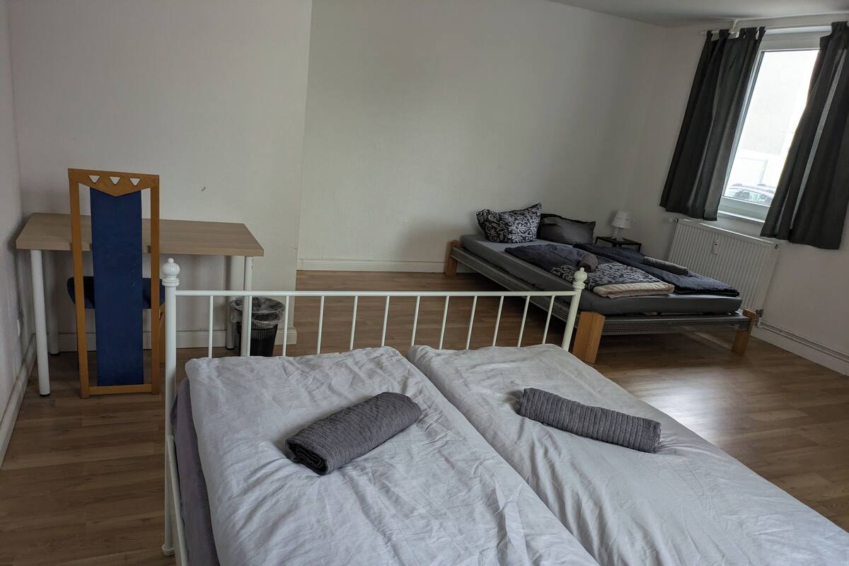 Ein Schlafzimmer mit zwei Betten, Holzboden, einem Fenster mit Vorhängen und einem kleinen Tisch mit Spiegel.