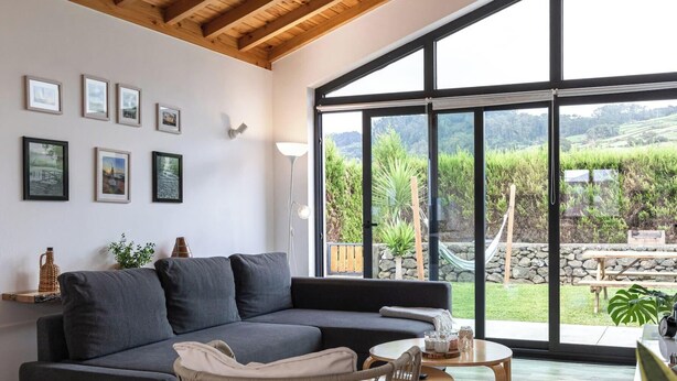 Ein modernes Wohnzimmer mit einem grauen Sofa, einem Korbstuhl und einem runden Holztisch.