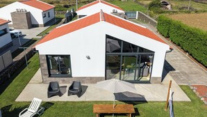 Ein modernes Haus mit weißer Fassade und rotem Dach, einer Terrasse mit Gartenmöbeln und Blick auf den Ozean.