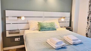 A neatly made bed with pillows, a bedside table, and a wall socket. - Casa da Gente T1 by PontaNegraAzores (Praia da Vitória)