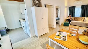 A modern kitchen with a washing machine, a dining area with a table and chairs, a sofa, and a large cabinet. - Casa da Gente T1 by PontaNegraAzores (Praia da Vitória)