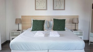 A hotel room with a large bed, two framed wall art pieces, a wooden headboard, two bedside tables with lamps, and neatly folded towels. - Casa da Gente T2 by PontaNegraAzores (Praia da Vitória)