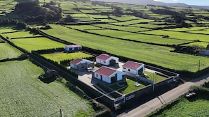 Una propiedad rural con tres edificios blancos, un muro de piedra y campos en terrazas.