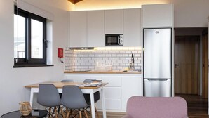 Cocina compacta con armarios blancos, un microondas y un refrigerador. Hay una mesa de comedor con sillas y una pequeña mesa redonda con una vela.