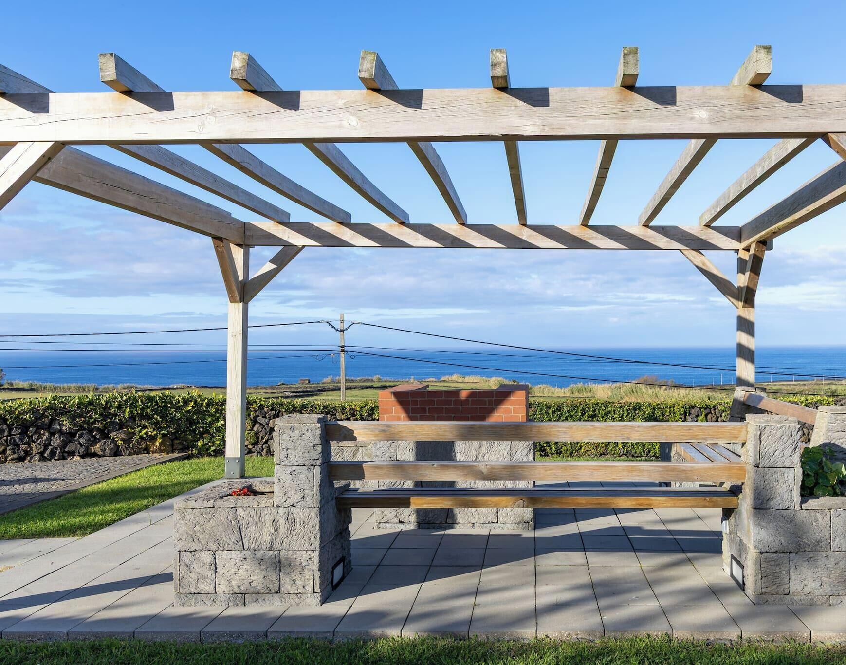 Una pergola in legno con una panca, pareti in pietra e vista sull'oceano.