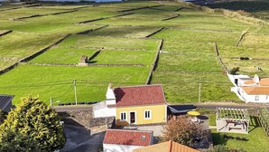 Ländliche Landschaft mit Feldern, einem Haus mit rotem Dach und Blick auf das Meer.