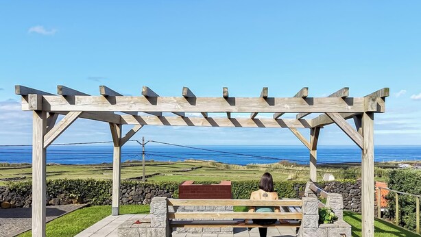 Eine Holzpergola mit einer Bank, mit Blick auf eine Küstenlandschaft und freiem Meerblick.