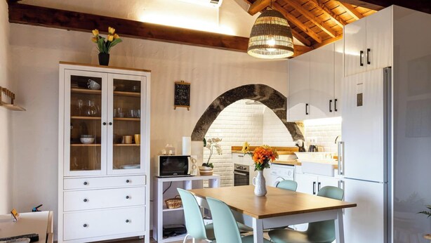 A compact kitchen with white cabinets, a wooden dining table, and a hanging light fixture. - Charming Country House by PontaNegraAzores (Angra do Heroísmo)
