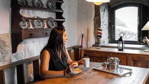 Una persona sentada a una mesa de madera con una bandeja de teteras y tazas, un mapa en la pared y una ventana con vistas a un paisaje nevado.