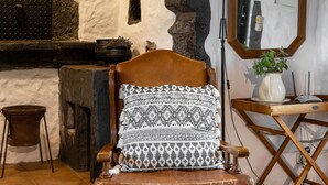 Una habitación rústica con una silla de madera, una chimenea de piedra, un espejo y una lámpara de pie.