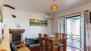 A cozy living room with a fireplace, wooden furniture, and a dining area with chairs. - Casa da Maresia - By Ponta Negra Azores (Praia da Vitória)