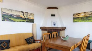 A dining area with a wooden table and chairs, a fireplace, and two landscape paintings on the walls.