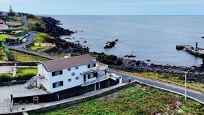A coastal building with a balcony, a paved road, and rocky shoreline. - Casa da Maresia - By Ponta Negra Azores (Praia da Vitória)