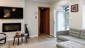 Una sala de estar con chimenea, un sofá, un televisor y una puerta que da a otra habitación.