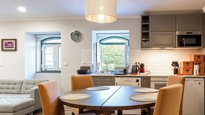 Una cocina moderna con comedor, que presenta una mesa redonda de madera con sillas, una lámpara colgante y vistas a través de las ventanas.