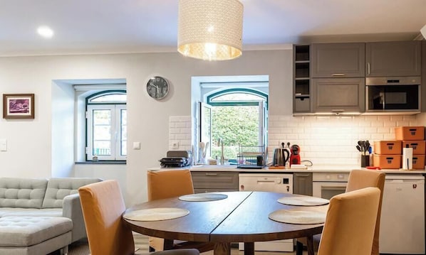 Cozinha moderna com área de refeições, apresentando uma mesa redonda de madeira com cadeiras, uma luminária pendente e vista pela janela.