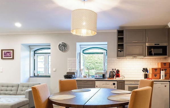 A modern kitchen with a dining area, a sofa, and a large window.
