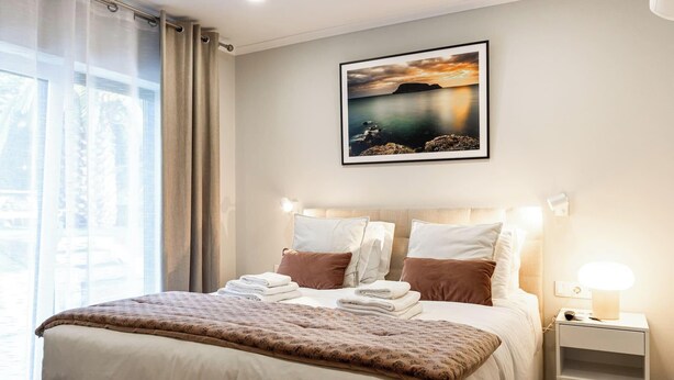 Habitación de hotel con cama, almohadas, mesita de noche, lámpara y un cuadro en la pared.