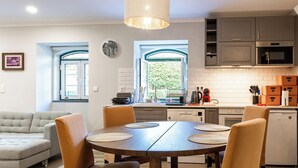 Una cocina moderna con comedor, que presenta una mesa redonda de madera con sillas, una lámpara colgante y vistas a través de las ventanas.