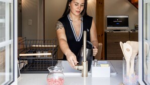 Una persona en una encimera de cocina con un fregadero, un escurreplatos, una lámpara colgante y una escalera al fondo.